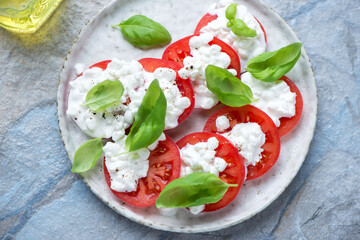 Cottage cheese caprese with ripe tomatoes and green basil, horizontal shot on a blue and beige stone background, high angle view