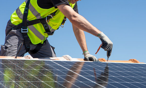 Workers install solar panels on a sunny day at a residential rooftop in an urban area