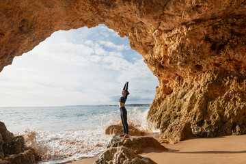 Woman practicing yoga in a cave by the sea