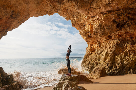 Woman practicing yoga in a cave by the sea