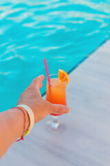 Cocktail in hands of woman against the background of swimming pool. Selective focus.
