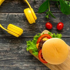 Flat lay of a cheeseburger with yellow headphones and fresh herbs