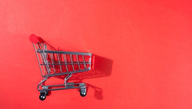 Flat lay composition of a mini metallic shopping trolley against a vivid red background, evoking themes of market activity, consumer choices, and purchasing power in a minimalist setting - Powered by Adobe