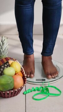 Vertical Video, Weight loss journey, African woman steps on scale with fruit basket. Health, diet, wellness concept.