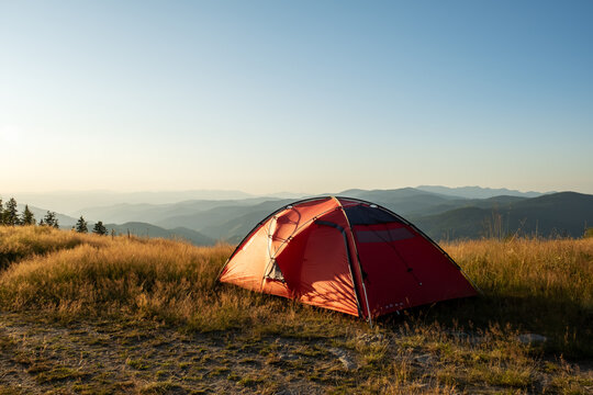 Morning mountain silence, red tent pitched on hill overlooking forested valleys, clean light and blue sky capture freedom and stillness of wild camping life, minimal gear, solo adventure story