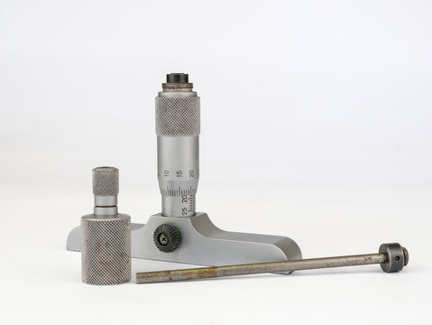 A disassembled depth micrometer is laid out on a clean white background. The precision measuring tool's main body, interchangeable measuring rod, and extra anvil on white background.