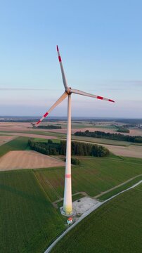 Luftaufnahme einer einzelnen Windturbine im Abendlicht, umgeben von Feldern und kleinen W&auml;ldchen, Symbol f&uuml;r erneuerbare Energie, Hochformat, 4K