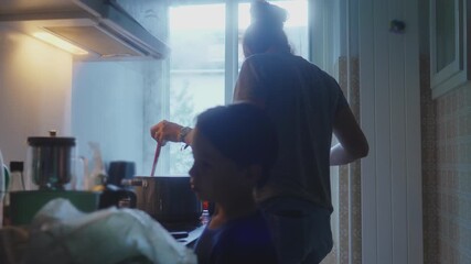 Mother stirring steaming pot while cooking dinner in kitchen as young son stands nearby, warm family evening routine creating cozy home atmosphere