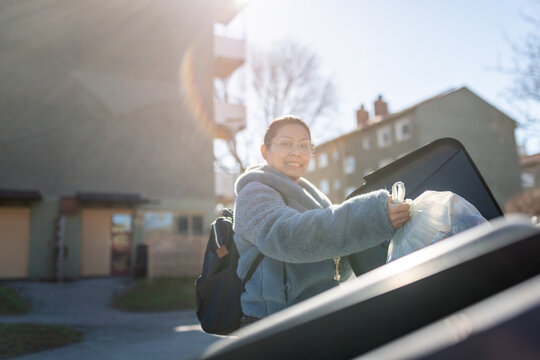 Portrait of smiling woman dumping garbage bag in bin at sunny day