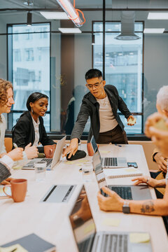 Young male business professional sticking adhesive note on table while discussing ideas with team in board room at office