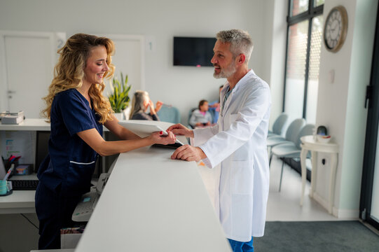 Nurse handing over medical records to doctor at reception desk in hospital waiting room, ensuring smooth patient care and information exchange