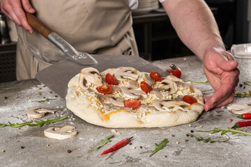 Culinary expert preparing a fresh pizza topped with mushrooms and cherry tomatoes, showcasing the artistry of pizza making in a professional kitchen environment