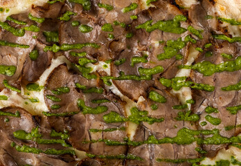 Close-up view of delicious roasted beef topped with vibrant green pesto sauce, showcasing rich textures and appetizing colors, perfect for culinary presentations and food photography