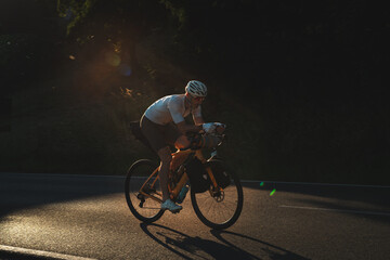Radfahrer fährt auf gelben Fahrrad und Gepäck auf der Strasse in den Sonnenuntergang, bikpacking, Radreise