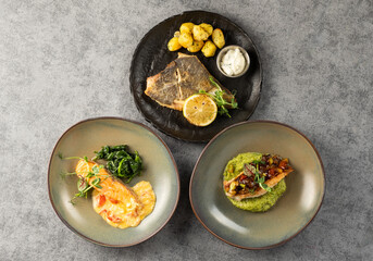 Gourmet plated fish dish with sides of seasoned potatoes, sauteed greens, and vibrant sauces, showcasing culinary artistry and modern dining presentation