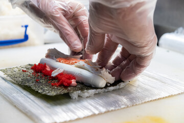 Asian chef skillfully preparing sushi rolls with fresh ingredients, including seafood and vegetables, on a bamboo mat in a modern kitchen setting, showcasing culinary artistry and precision