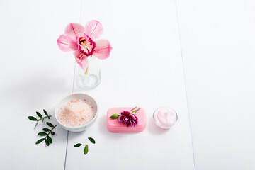 cosmetic cream, soap and bath salt with pink flower, white wood table