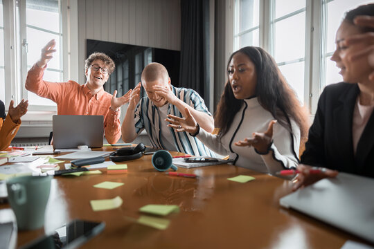 Male business employees reacting on female colleague spilling coffee on table in meeting room