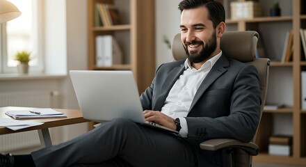 Man in suit smiling at laptop in office with bookshelves and window