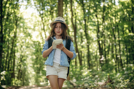 Small notepad is in hands. Young girl hiker is in the forest