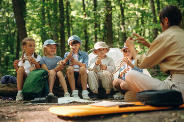 Survival tips, sitting at camp. Woman is doing tour for group of kids in the forest