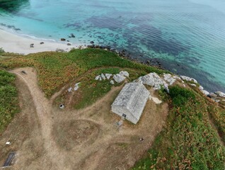 Aerial drone view of the historic coastal watch house near Guissény, France. Perched on cliffs above the Atlantic, surrounded by Natura 2000 wetlands and walking trails.