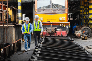 Two engineer wearing safety gear walking through a railway maintenance, inspecting train parts and infrastructure. Concept of industrial safety, rail engineering and station inspection.