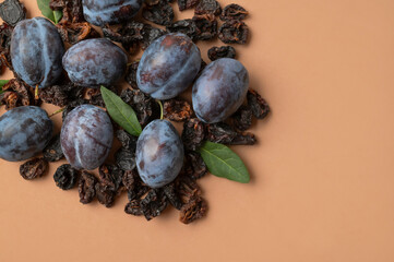 Dried plum prunes and fresh plums with green leaves on brown background flat lay top view. Food background, dried delicious fruits, sweet healthy dessert, healthy eating