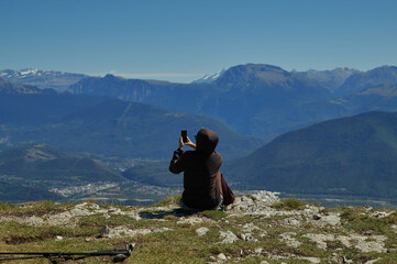 Traveler taking smartphone photo of alpine mountain landscape from rocky peak