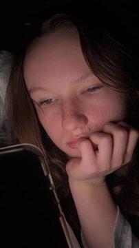 Teen girl lying in bed at night using smartphone, scrolling social media and texting. Not healthy sleep. Insomnia and the harm of the smartphone before going to bed. Dependence on social networks