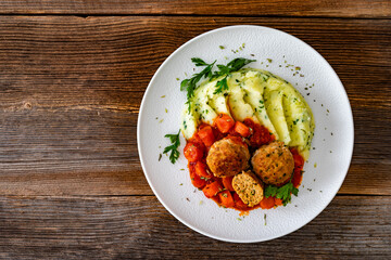 Fried pork meatballs and carrots in tomato sauce with mashed potatoes on wooden table