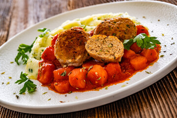 Fried pork meatballs and carrots in tomato sauce with mashed potatoes on wooden table