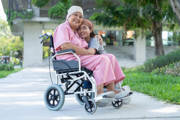 Asian careful caregiver or nurse and woman with cancer is sitting in a wheelchair. in the garden. Concept of happy retirement with care from a caregiver and Savings and senior health insurance.