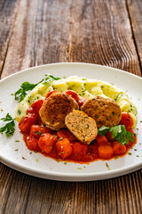 Fried pork meatballs and carrots in tomato sauce with mashed potatoes on wooden table