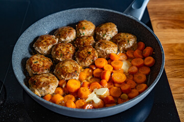 Frying pork meatballs and carrots in frying pan on electric stove