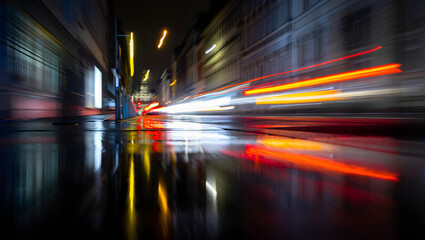 Blurred car lights streak through a city street at night, creating a vibrant and dynamic scene of urban life and transportation