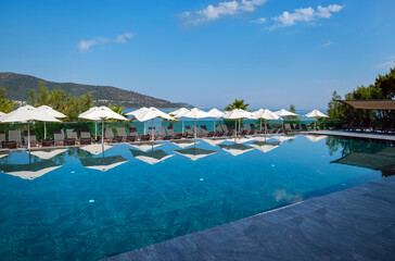 White umbrellas with shadows around outdoor luxury swimming pool 