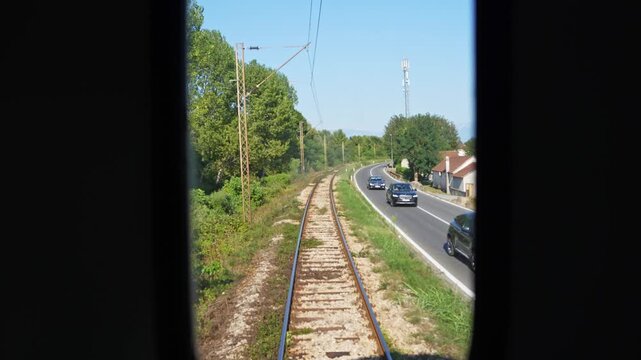 Train rear view with railway tracks. Rear view of a train showing railway tracks and a parallel road with cars. Railway transport through scenic countryside.