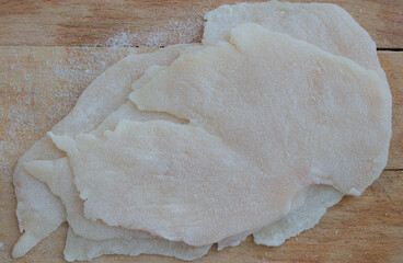 Chicken slices breaded with flour on a wooden cutting board