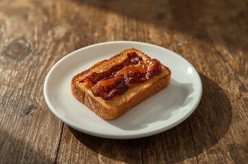 Crispy bacon-topped toast served on a white dish over a rustic wooden table