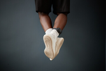 Feet of Black young adult man hanging on pull up bar against dark background wearing electronic...
