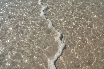 Sunny day beach scene with footprints on wet sand by the sea shore.