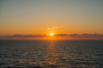 Obraz premium Breathtaking dawn over the ocean with waves gently lapping the shore. Intimate morning by the beach. Early sunlight piercing through misty skies in a golden glow. Exploration and nature scene.