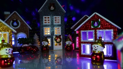 Many decorated houses and snowmen in an evening Christmas town with flying lights in the background