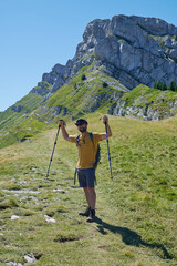 Smiling hiker raising trekking poles on alpine trail in Vercors Massif French Alps
