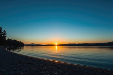 Obraz premium Dusk at the lakeshore with a yellow sun and blue sky mirrored on the water in a natural northern landscape