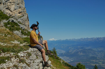 Hiker resting on rocky cliff in Vercors Massif with distant Mont Blanc view in French Alps