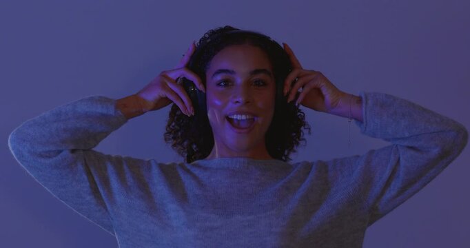 Video clip of a young adult female smiling and dancing in the studio while listening to music through wireless headphones. She has brunette curly hair and she is illuminated by colourful neon disco li