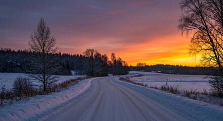 Journey through a vibrant winter sunset along a snow-covered country road