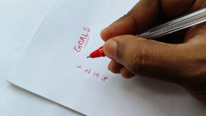 Closeup of hand with red pen underline word goals written on white paper. Ambition, planning, setting goal, aspirations, personal development and motivation concept.